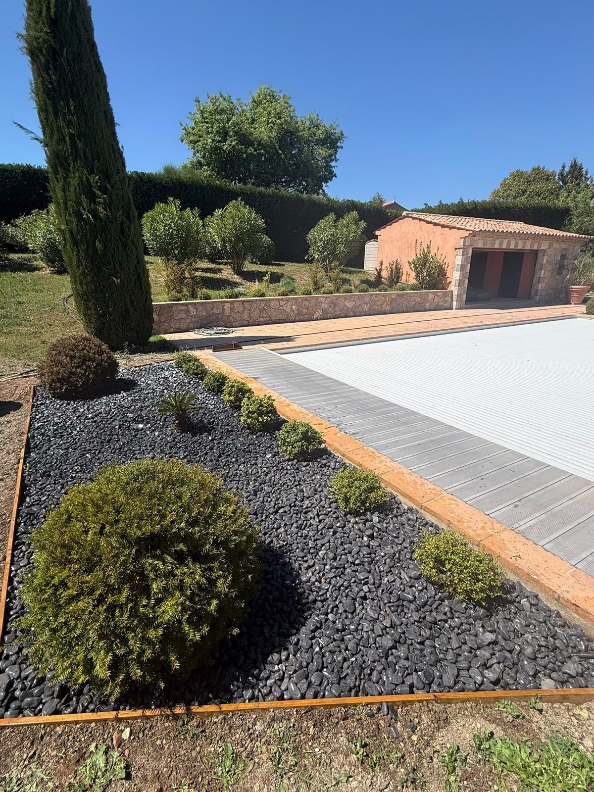 Massif minéral en ardoise noire avec boules de buis et bordure en acier, le long d'une piscine